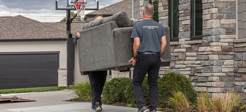 Delivery persons carrying a sofa to the front door of a customers home
