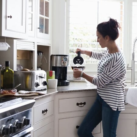 Woman pouring coffee from a drip coffee maker appliance into a mug